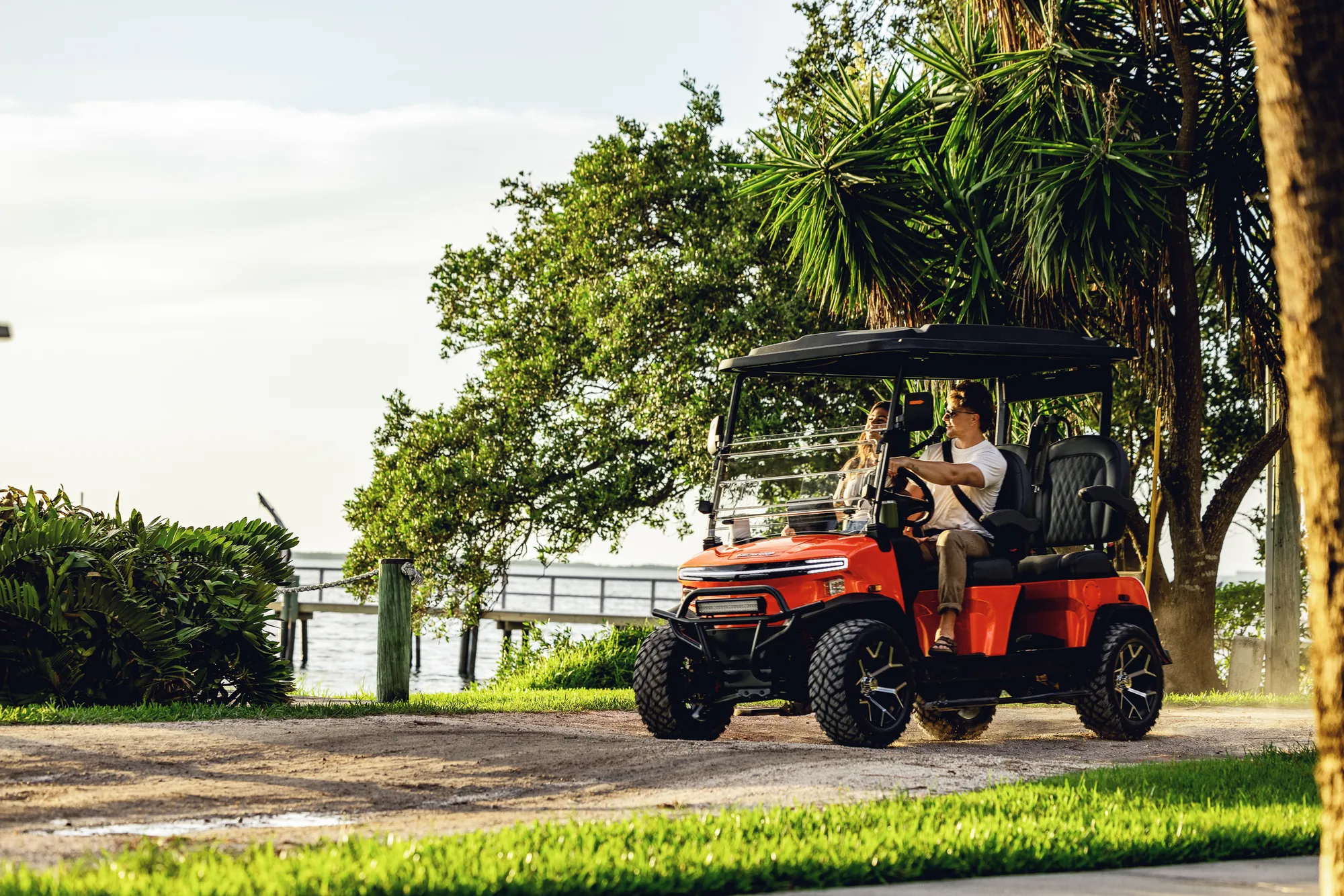 Couple driving an orange golf cart along the waterfront
