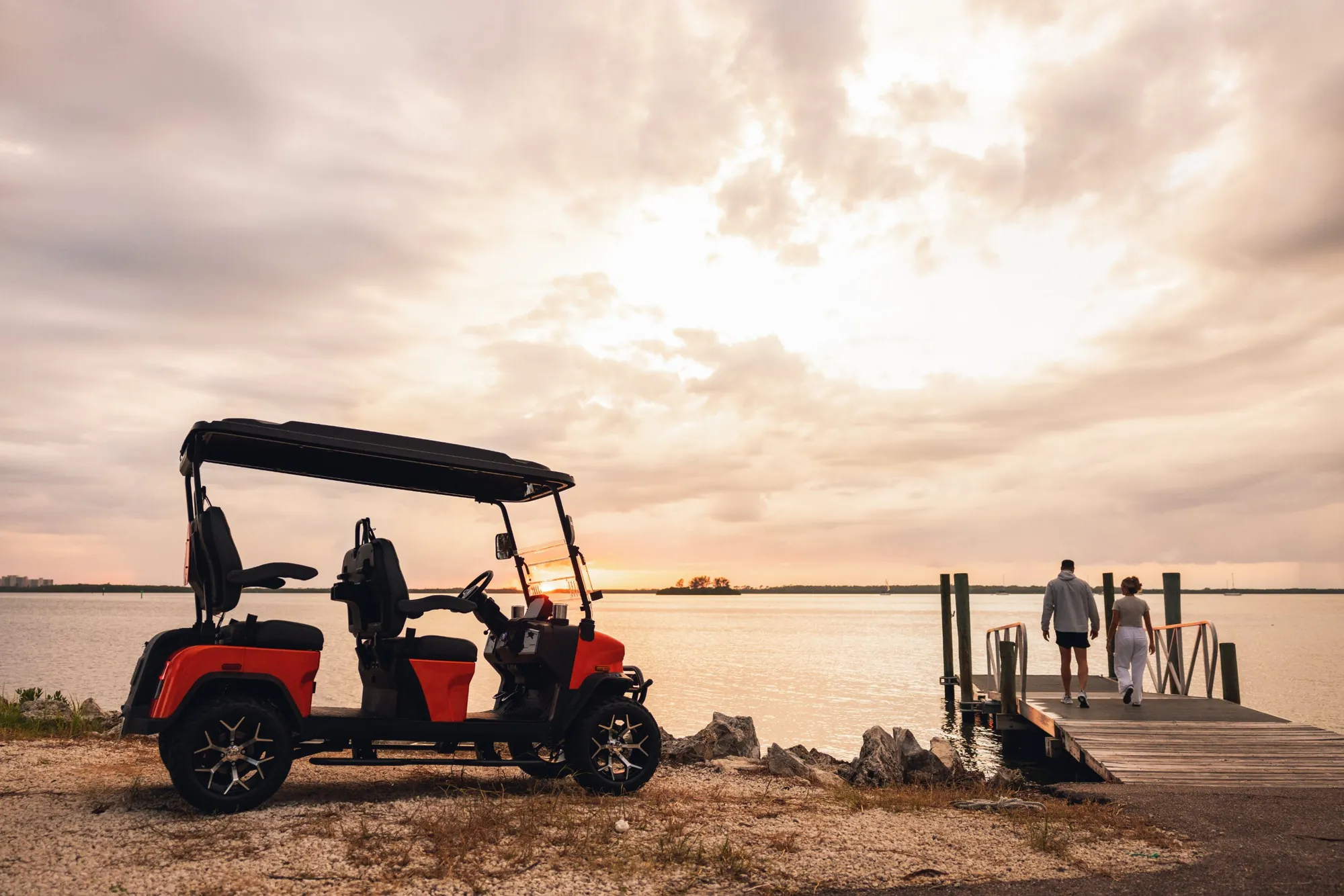 Orange Denago golf cart parked by the water at sunset